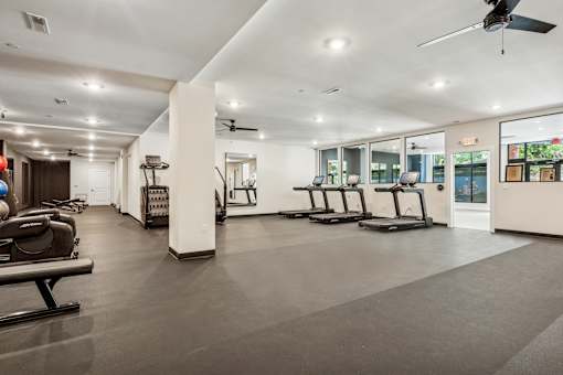 A spacious gym with treadmills, elliptical machines, and a ceiling fan.