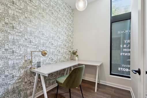 A white desk with a green chair in front of a wall with a mosaic of buildings.