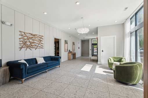 A spacious waiting area with a blue sofa, green armchair, and a wooden wall art.