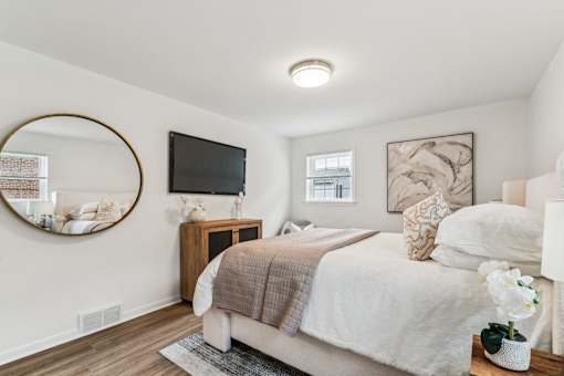 A bedroom with a bed, a round mirror, a TV, and a vase of flowers.