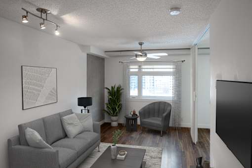 A living room with a grey couch, a grey armchair, a coffee table, a potted plant, and a painting on the wall.