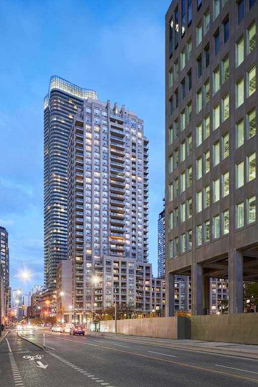 A tall building with a curved top stands next to a shorter building with a grid-like facade.