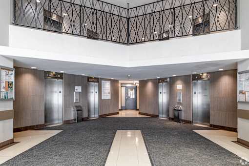 A hallway with a black metal railing and a row of elevators.