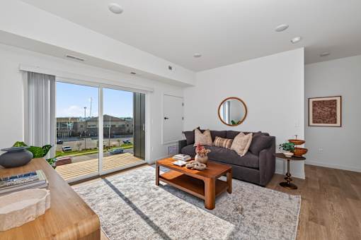 A living room with a grey couch, a wooden coffee table, and a round mirror on the wall.