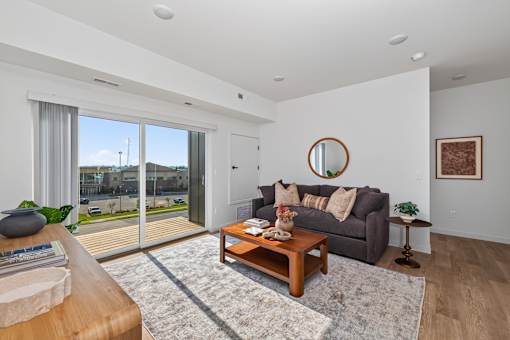 A living room with a grey couch, a wooden coffee table, and a round mirror on the wall.