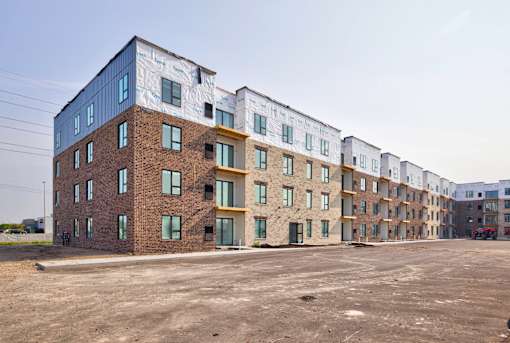 A row of multi-story apartment buildings with a parking lot in front.