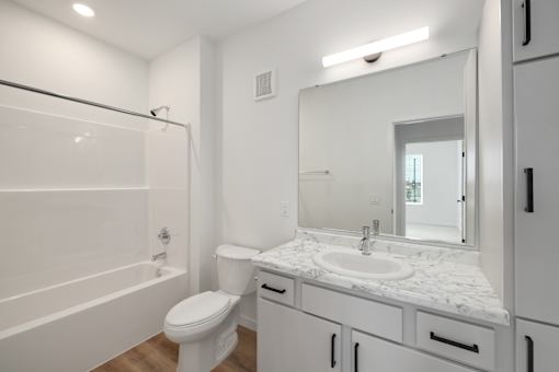 A white bathroom with a marble countertop and a large mirror.