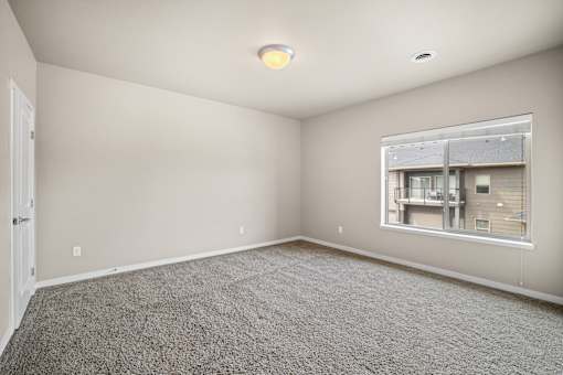 A room with a carpeted floor and a window showing a view of a building.