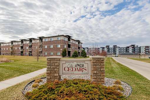 The Cedars apartment complex is surrounded by a well-maintained lawn and a clear sky.