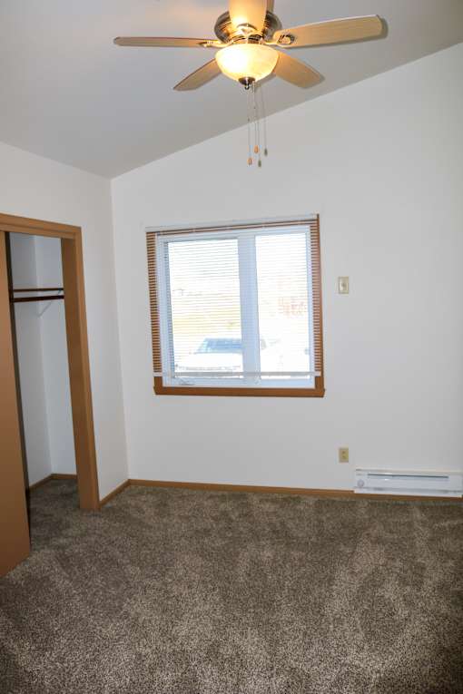 A room with a ceiling fan and a window with blinds.