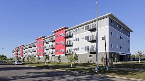 A street view of a multi-story building with red and grey sections.