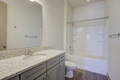 A white bathroom with a marble counter top and a walk in shower.
