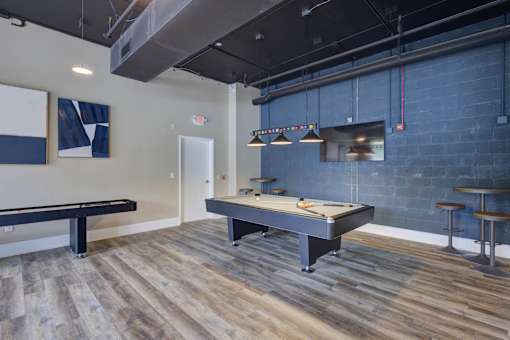 A pool table is in the middle of a room with a bench and a bar stool.