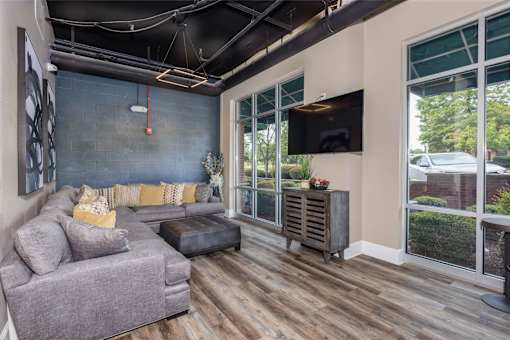 A grey couch with a black leather ottoman in front of a grey wall with a TV mounted on it.