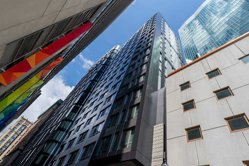 A tall building with a glass facade stands in front of a building with a white facade and a blue sky in the background.