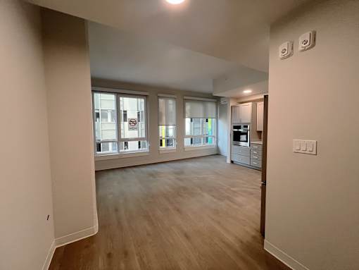A spacious room with wooden flooring and a kitchen area in the background.