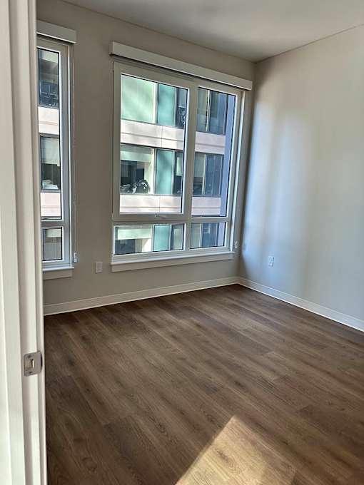 A room with a wooden floor and a window overlooking a building.