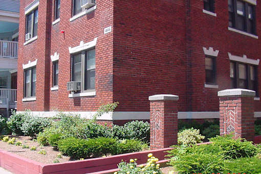 A red brick building with a white window and a small white pillar in front of it.