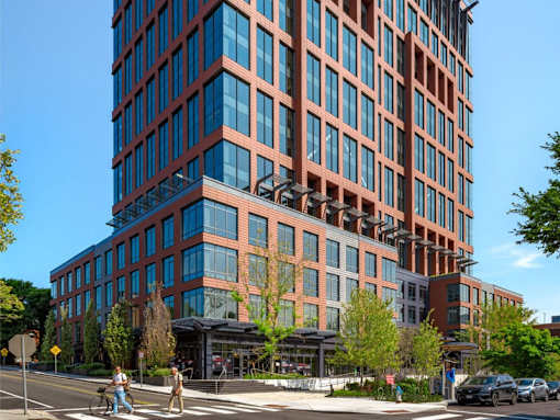 A tall building with a red and blue facade stands next to a street with cars and pedestrians.
