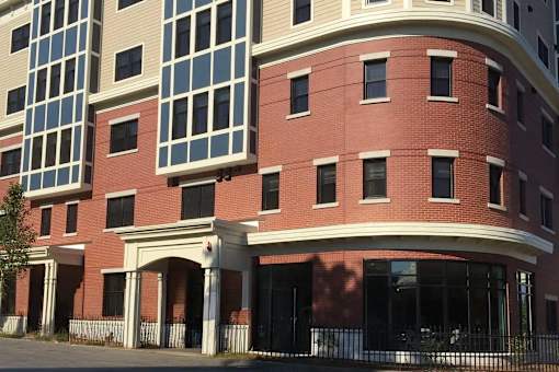 A red brick building with a curved corner and a black fence in front.