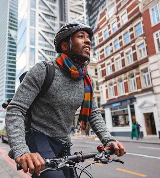 A man wearing a grey sweater and a multicolored scarf is riding a bicycle on a city street.