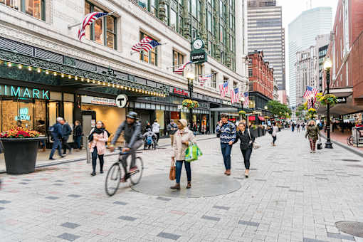 A busy street scene with people walking and a cyclist.