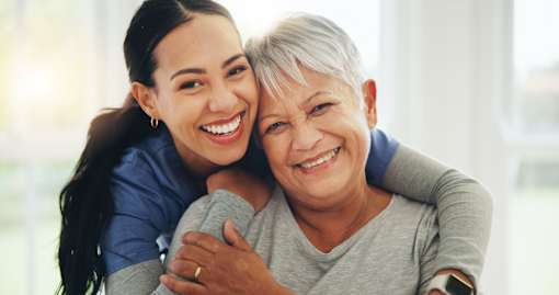 A woman with grey hair is hugging a younger woman.