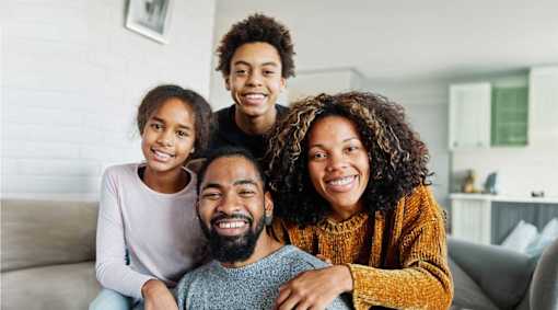 A family of four is sitting closely together on a couch.