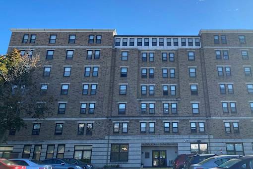 A large brick building with many windows and cars parked in front.