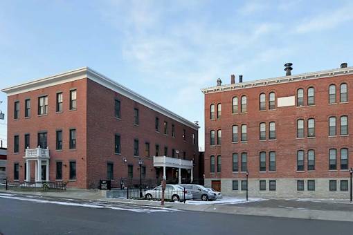 Two red brick buildings with white trim and a car parked in front of them.