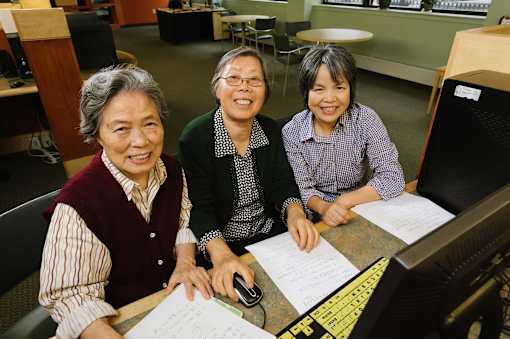 Three people are sitting at a desk with papers and a computer.