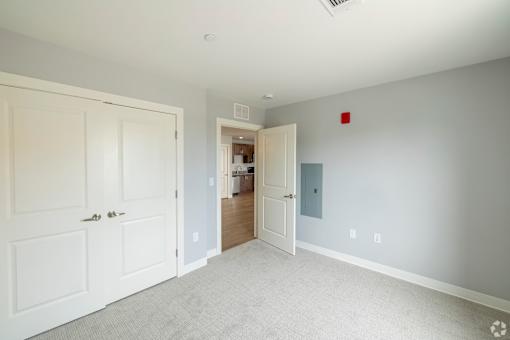 A room with a white door and a grey carpet.