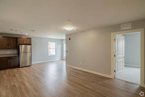 A spacious room with wooden flooring and a kitchen area to the left.