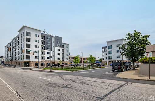 A street view of a residential area with apartment buildings and cars parked on the side of the road.