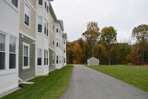 A long road with a white house on the right and apartment buildings on the left.