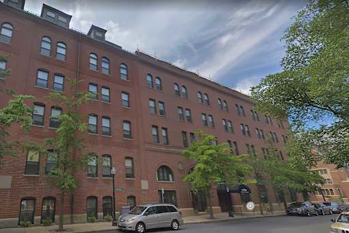 A street view of a red brick building with a silver van parked in front.