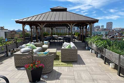 A gazebo on a rooftop patio with wicker furniture and potted plants.
