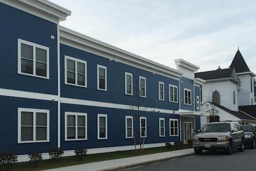 A blue building with white trim and a white church in the background.