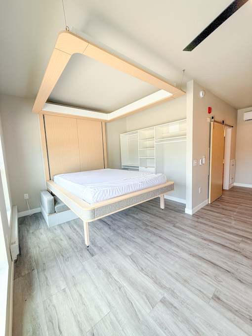 A bed with a wooden frame and mattress is in a room with a wooden floor and a ceiling with a skylight.