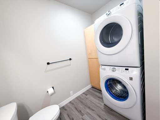 A white washing machine sits in a laundry room next to a toilet.