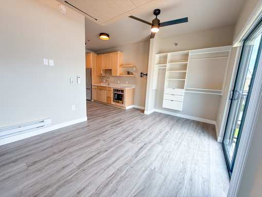 A room with a ceiling fan and a kitchen area in the background.