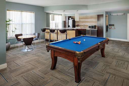 A pool table in a room with a bar and kitchen in the background.