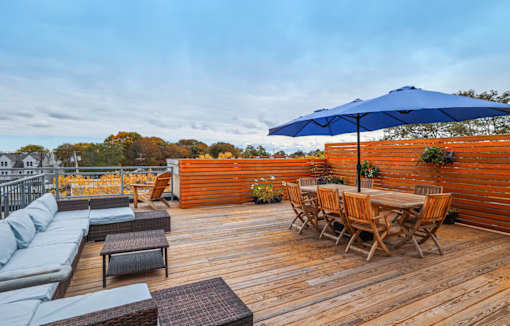 A wooden deck with a table and chairs under a blue umbrella.
