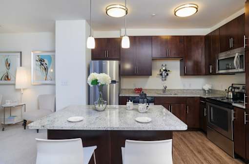 A kitchen with a table and chairs in the foreground and a refrigerator, microwave, and oven in the background.