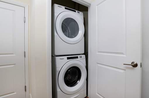 A white door is open to reveal a stack of white washing machines.
