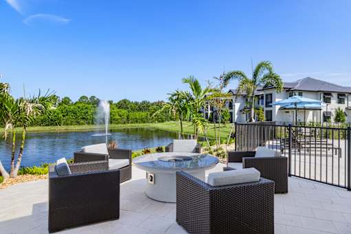 a patio with chairs and a fire pit overlooking a pond and a fountain