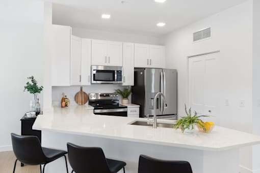 a kitchen with a large island with black chairs and a stainless steel refrigerator
