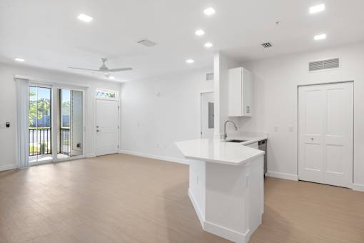 an empty living room with a kitchen and a balcony