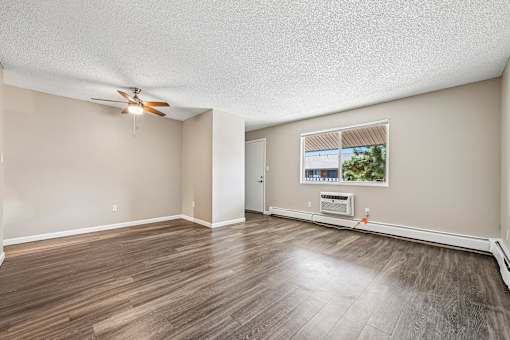 A room with a ceiling fan and a window with a view of trees and a house.