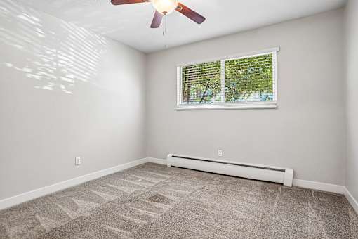 A room with a carpet floor, a ceiling fan, and a window with blinds.